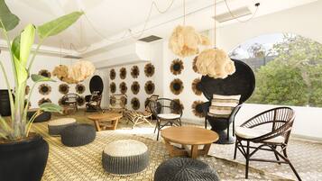 A modern living room with a large potted plant, round ottomans, a wooden coffee table, and multiple wicker chairs.