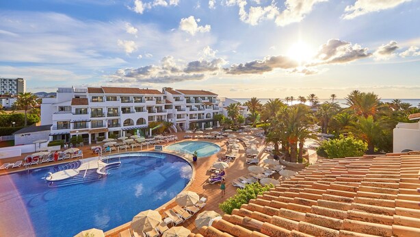 Un resort con una gran piscina, varias zonas de descanso y vista al mar.