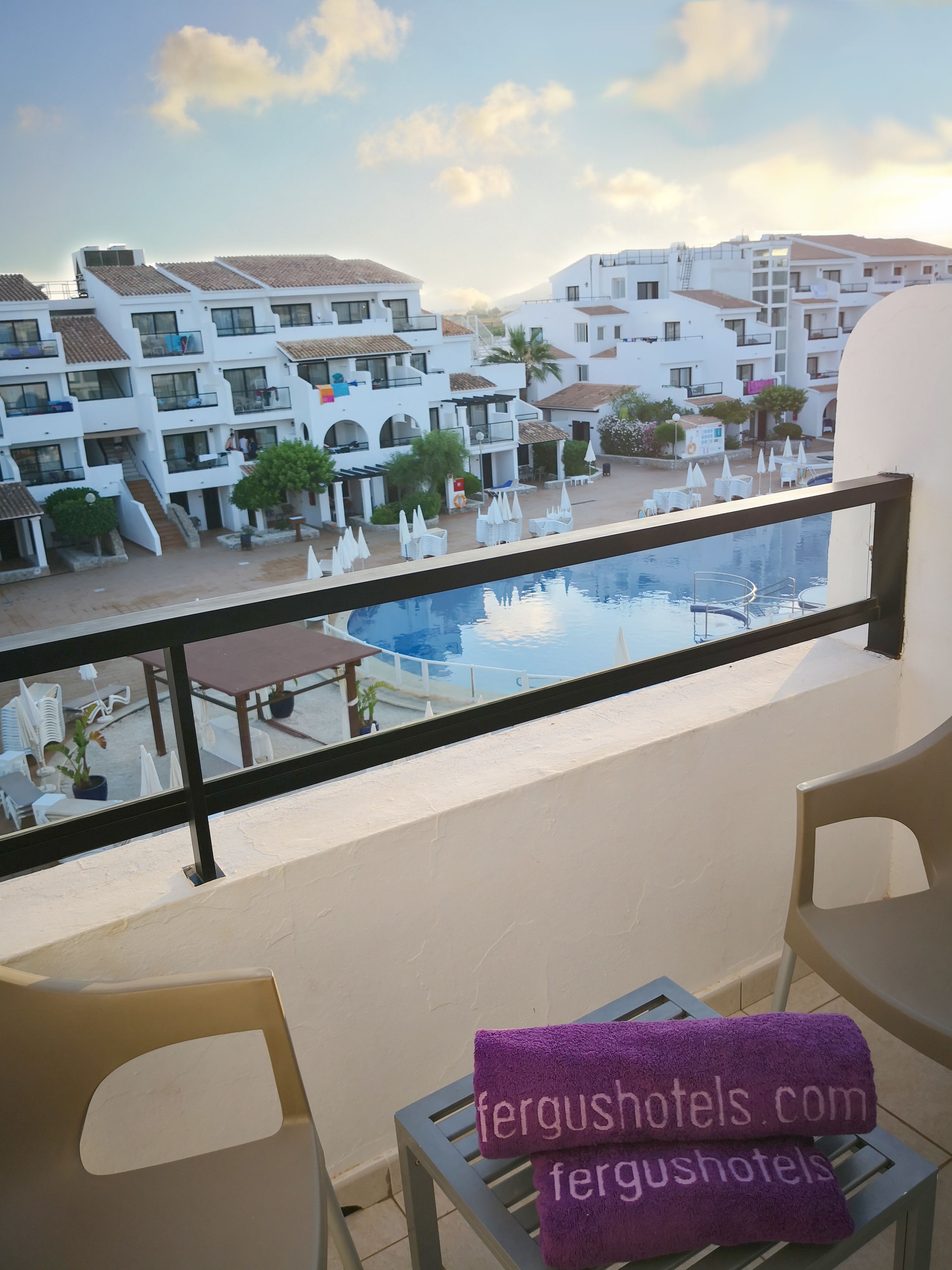 A balcony with a view of a swimming pool, white buildings, and a clear sky.