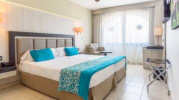 A hotel room with a large bed, a desk, a chair, and a TV.