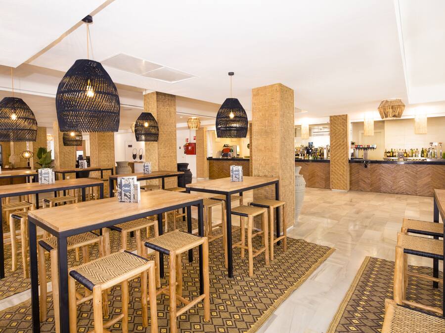 Um restaurante com mesas e cadeiras de madeira, luminárias negras pendentes e piso em padrão herringbone.