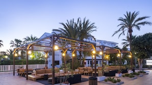 Un espacio al aire libre con patio, mobiliario, una pérgola y plantas en macetas.