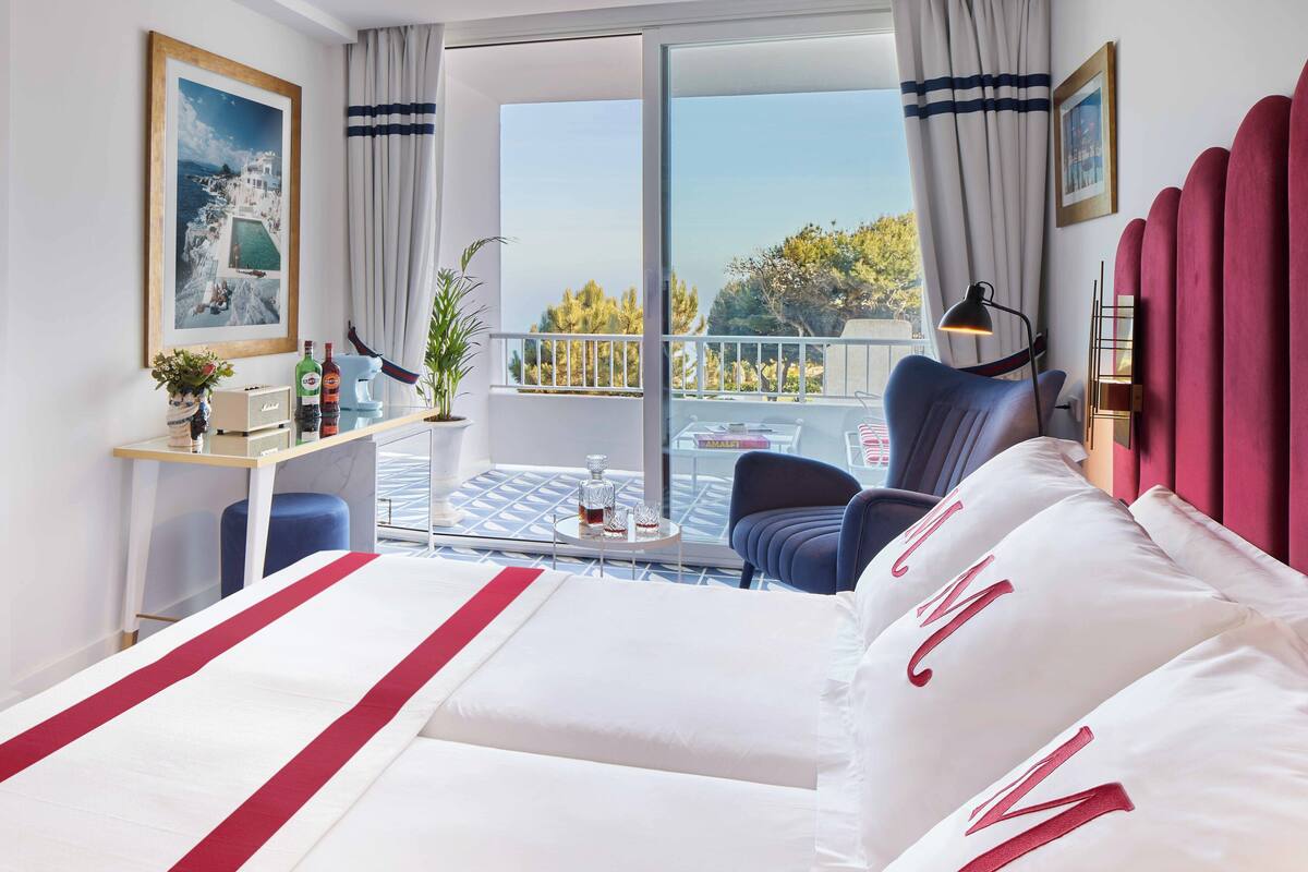 A hotel room with a large bed, a balcony with a table and chairs, and a view of the outdoors.