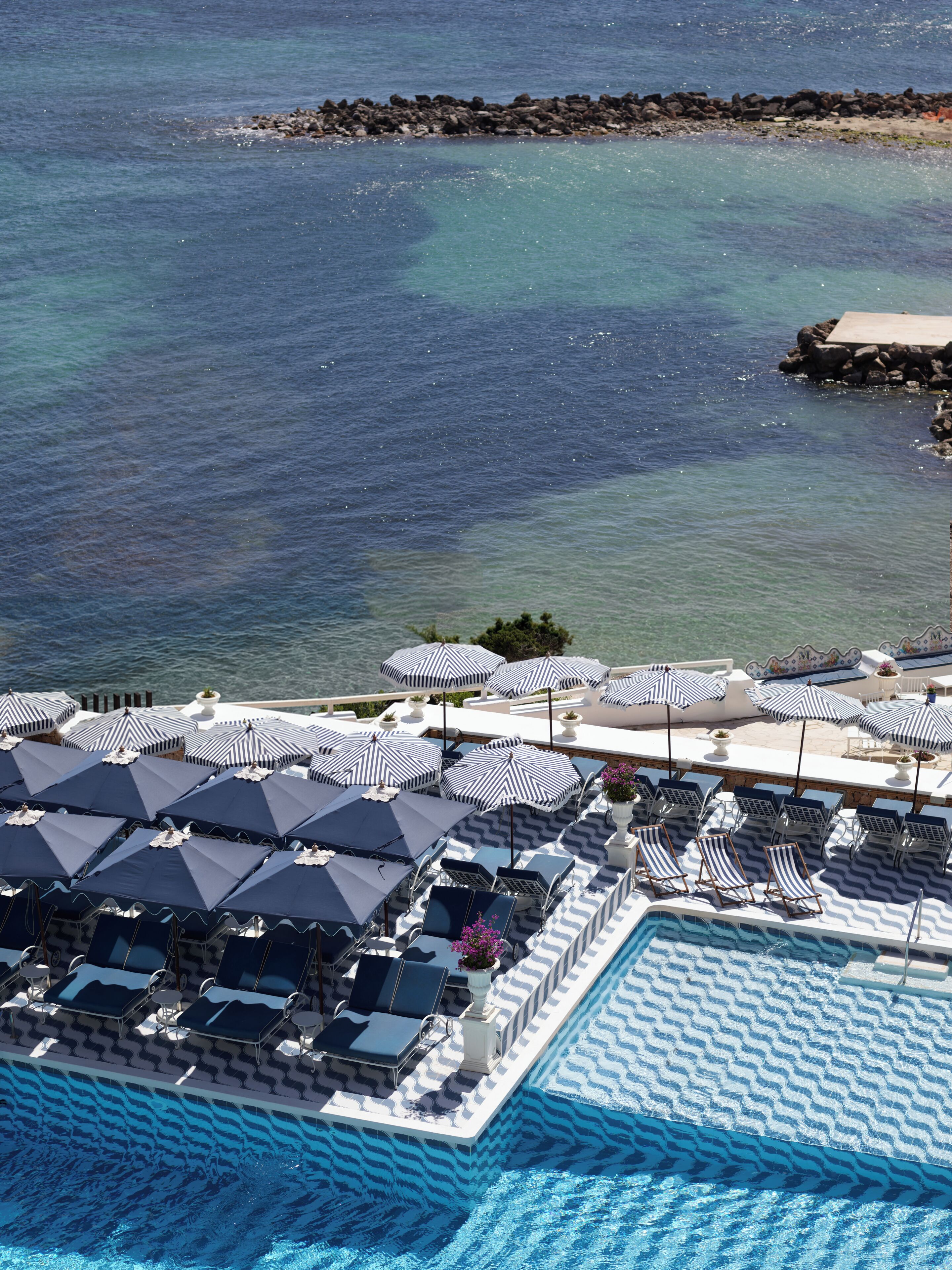 A poolside area with lounge chairs and umbrellas, overlooking a body of water.