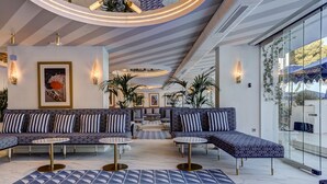 Ein moderner Loungebereich mit gemusterten Sofas, runden Tischen und Blick durch eine Glaswand.