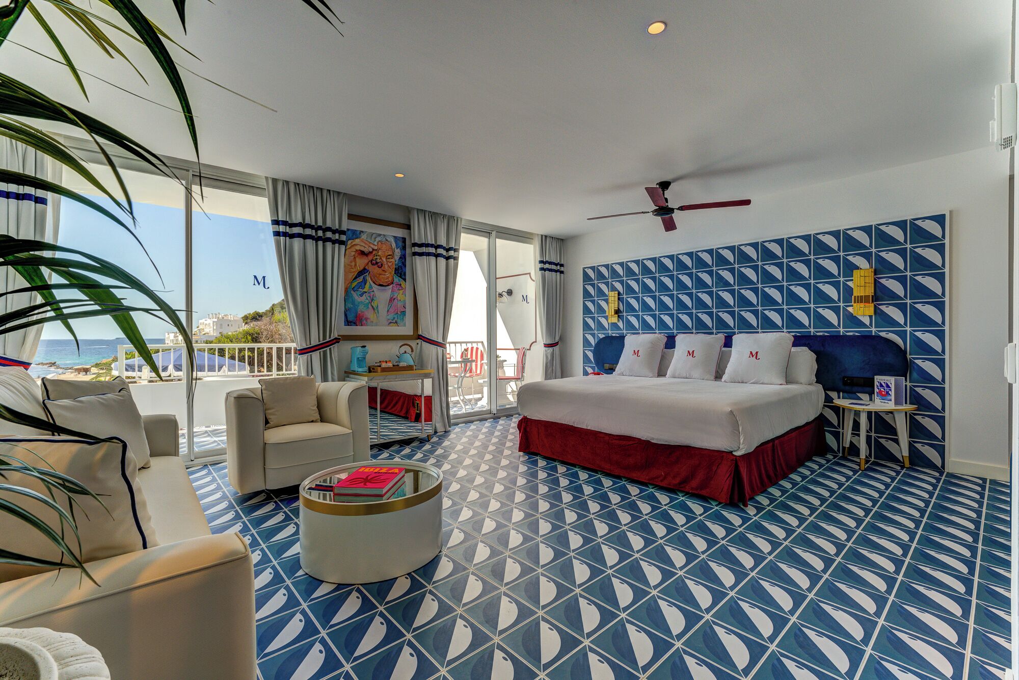 Ein Hotelzimmer mit einem großen Bett, einem Deckenventilator, Meerblick und einem gemusterten Boden.