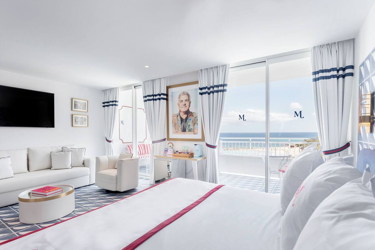 A modern hotel room with a large bed, a desk, and a view of the ocean.