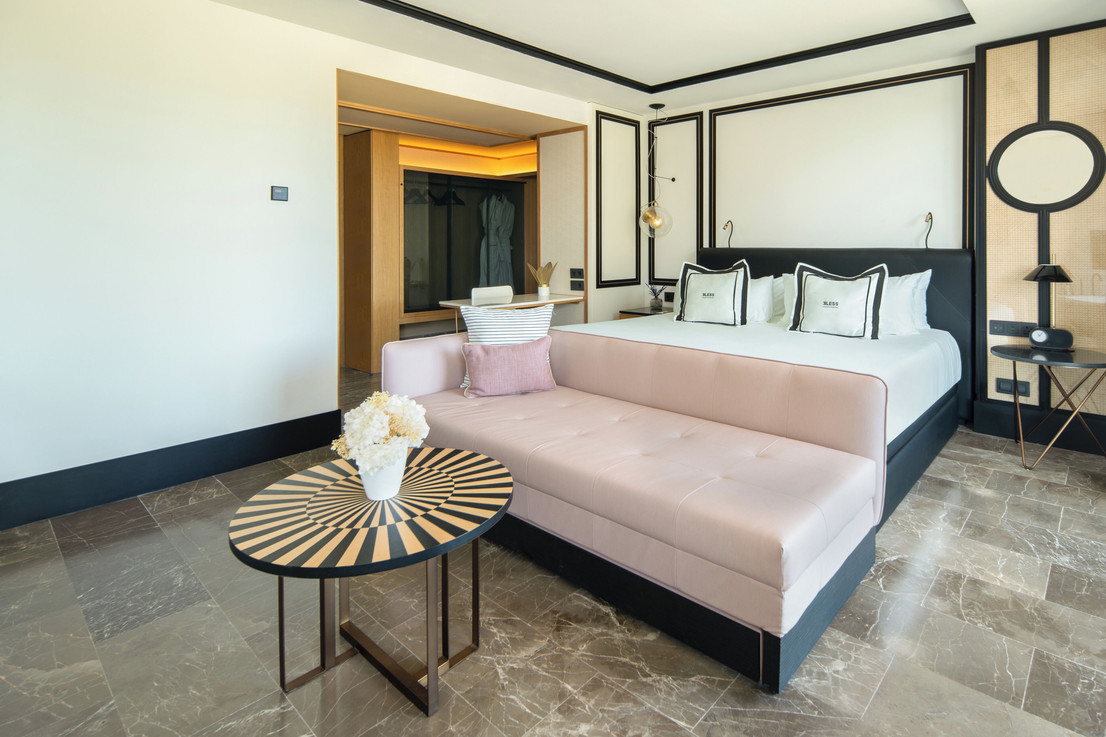 Une chambre d’hôtel moderne avec un grand lit, un canapé, une petite table ronde et un miroir.