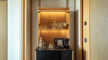 A compact minibar with a coffee maker, glasses, and a bottle.