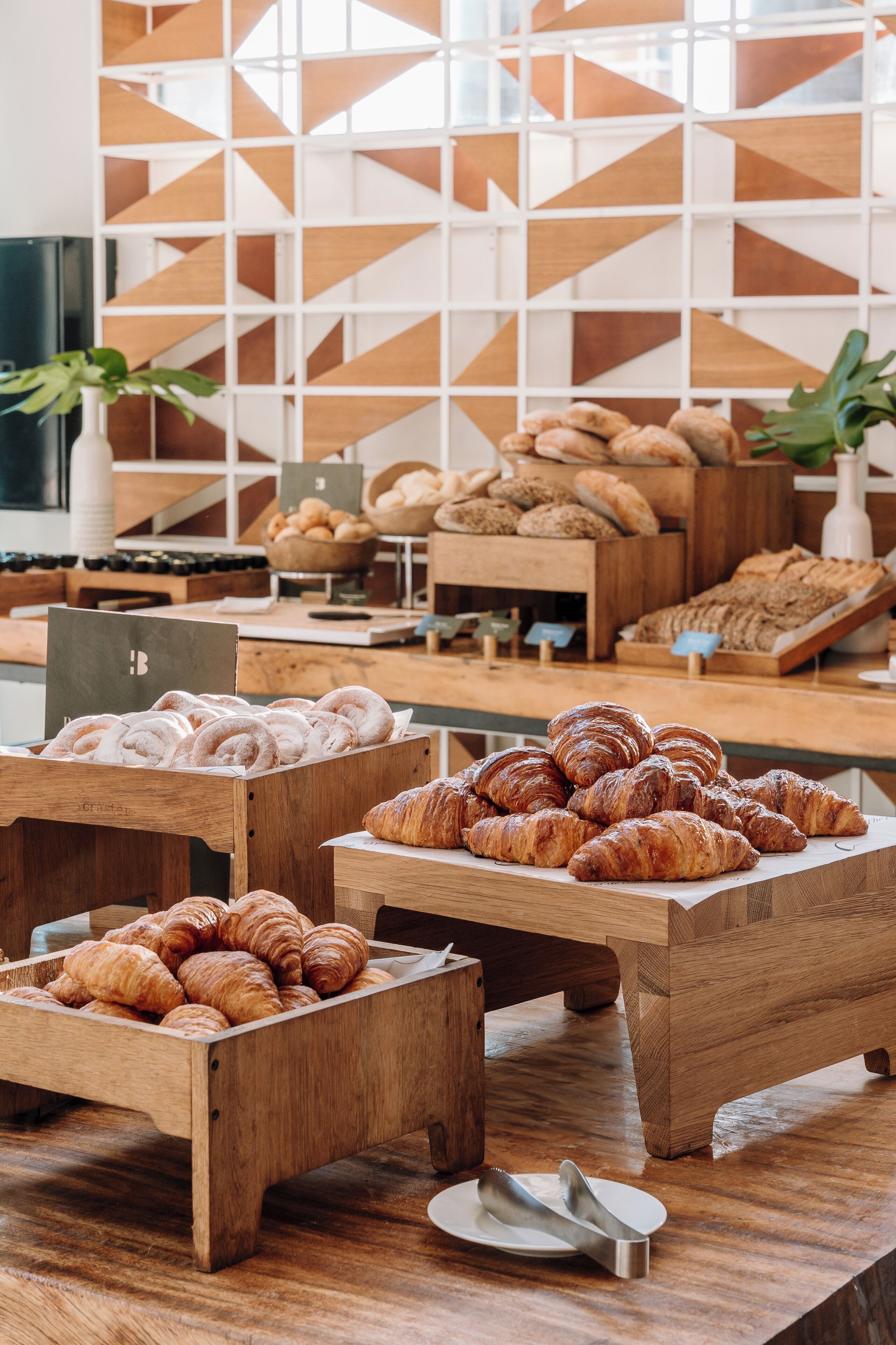 A bakery display with various baked goods, wooden stands, and a geometric wall design in the background.