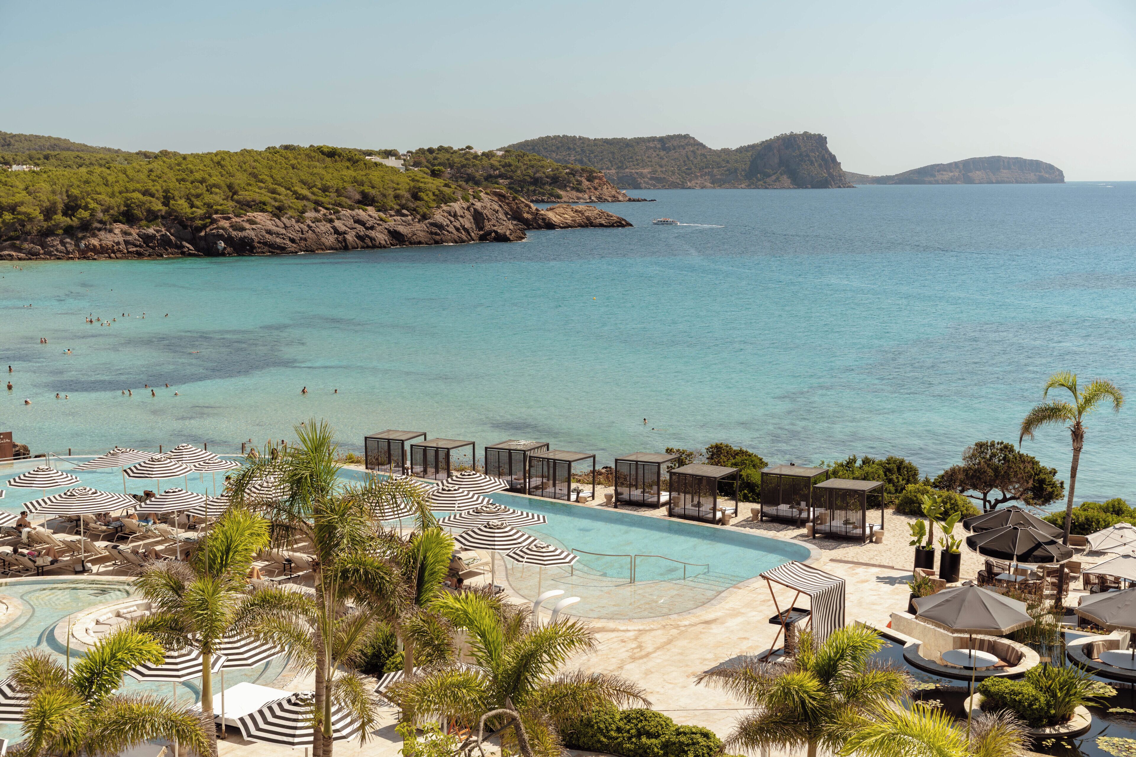 Ein Resort mit Swimmingpool, Strandbereich und Blick auf Meer und Hügel.