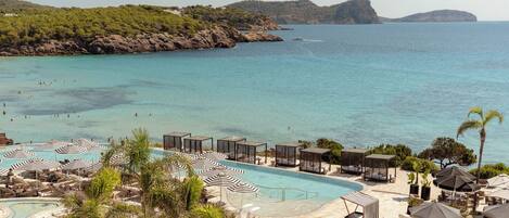 Ein Resort mit Swimmingpool, Strandbereich und Blick auf Meer und Hügel.