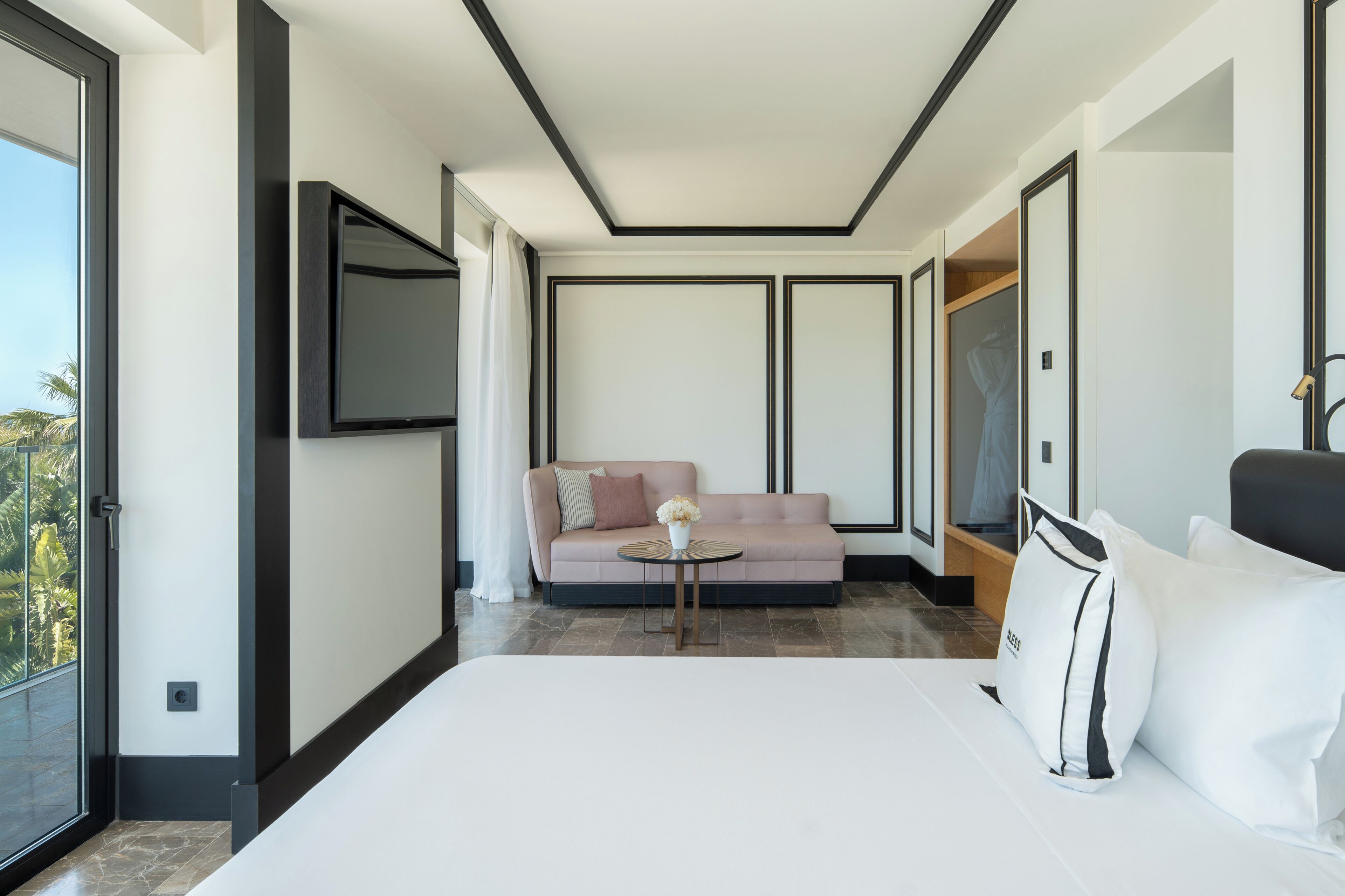 Een moderne hotelkamer met een groot bed, een bank, een klein rond tafeltje met een vaas en een aan de muur bevestigde televisie.