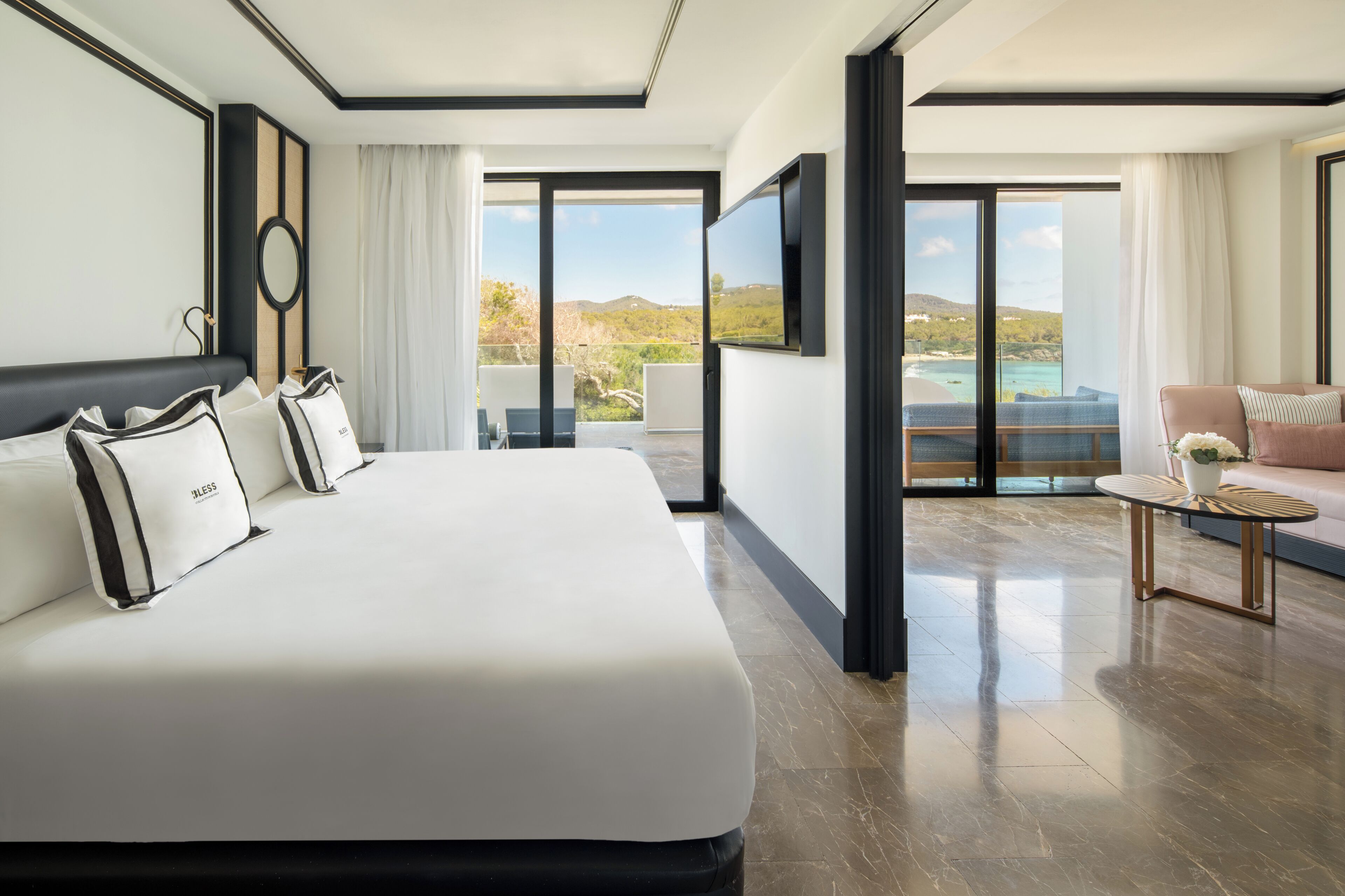 A modern hotel room with a large bed, a small table, and a balcony with a view of the sea.
