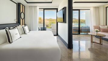 A modern hotel room with a large bed, a small table, and a balcony with a view of the sea.