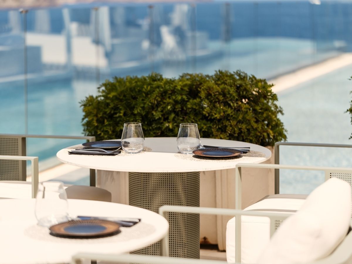 A round table with a white tablecloth, two glasses, and a plate set for two.