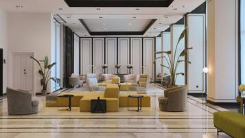 A spacious lobby with a modern design, featuring a central seating area with yellow sofas and chairs, a high ceiling with recessed lighting, and large windows allowing natural light.