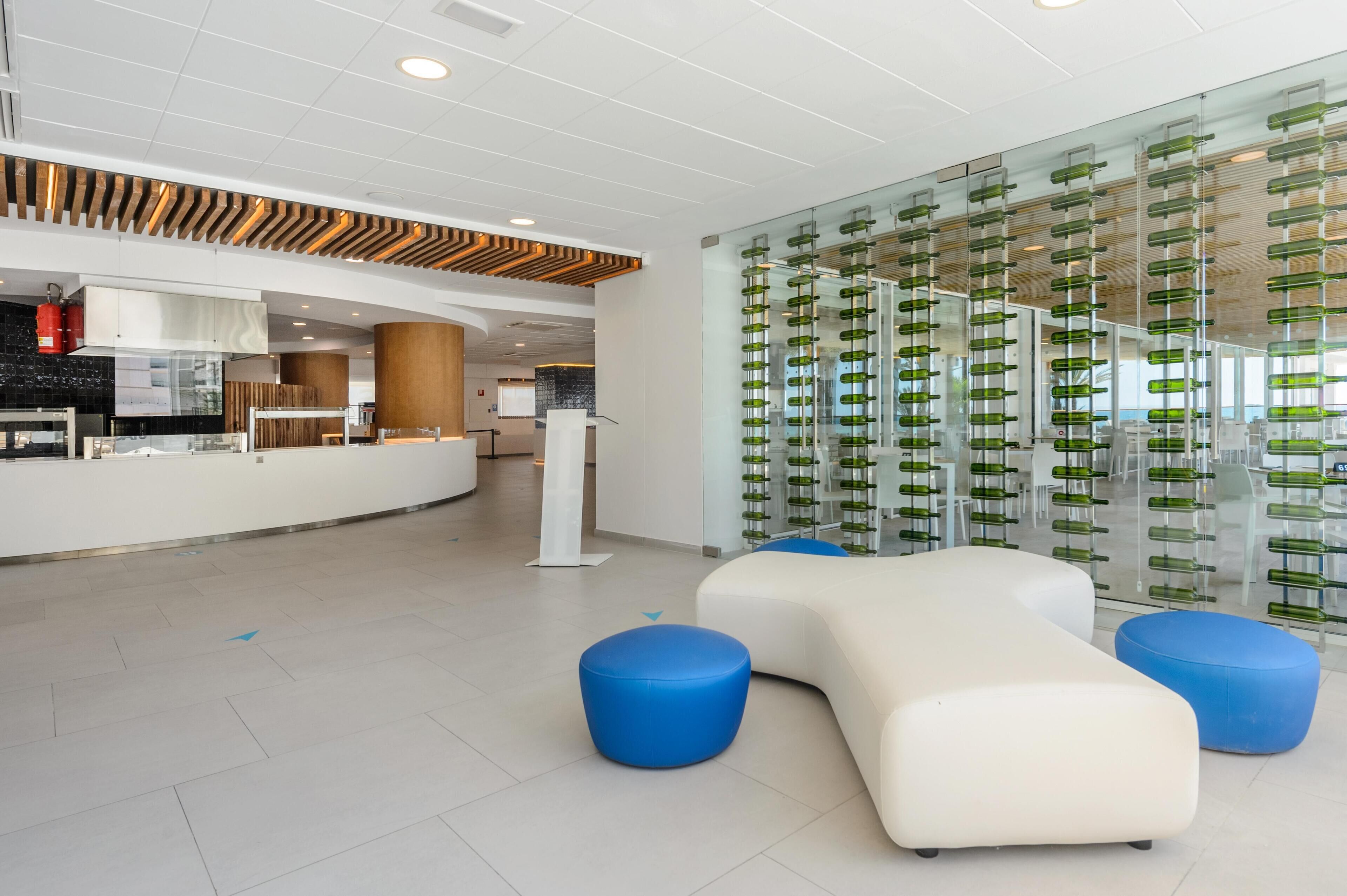 A modern lobby with a reception desk, seating area, and a wall with green bottles.