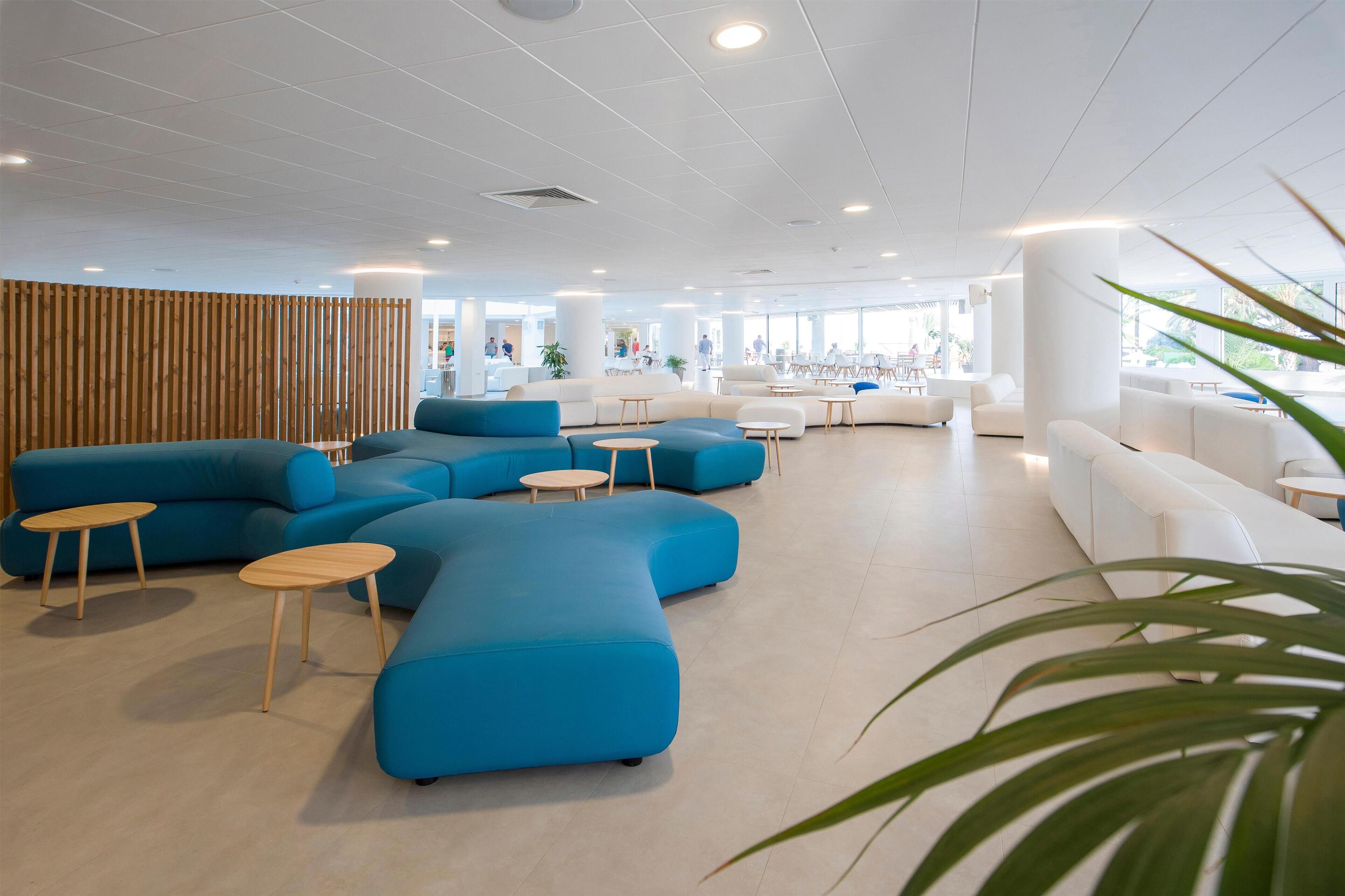 Eine geräumige Lobby mit blau-weißen Sitzbereichen, Holzelementen und einem großen Fenster, das für natürliches Licht sorgt.