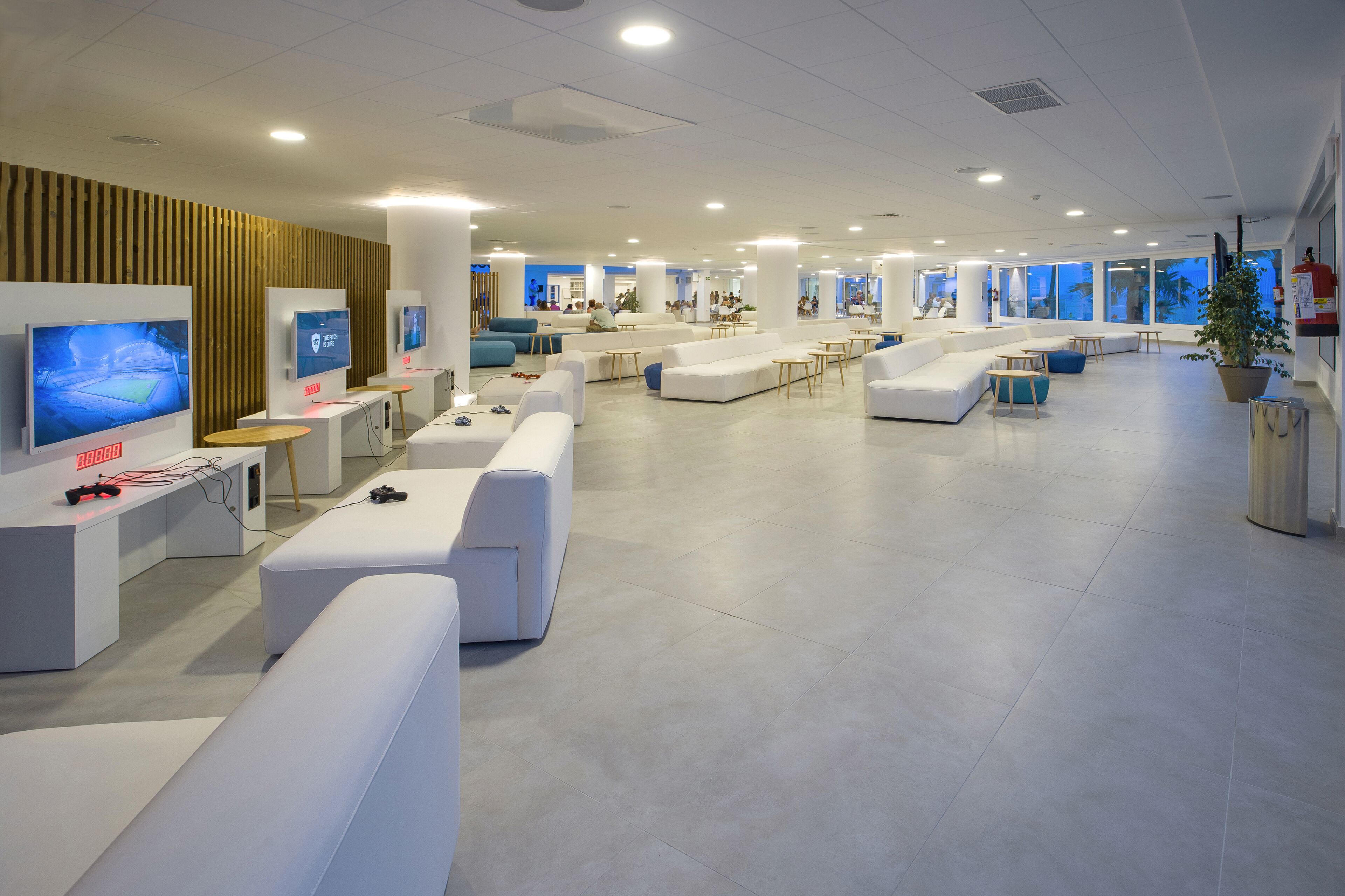 Eine moderne, geräumige Lobby mit weißen Sofas, einem Empfangsbereich und großen Fenstern mit Blick nach außen.
