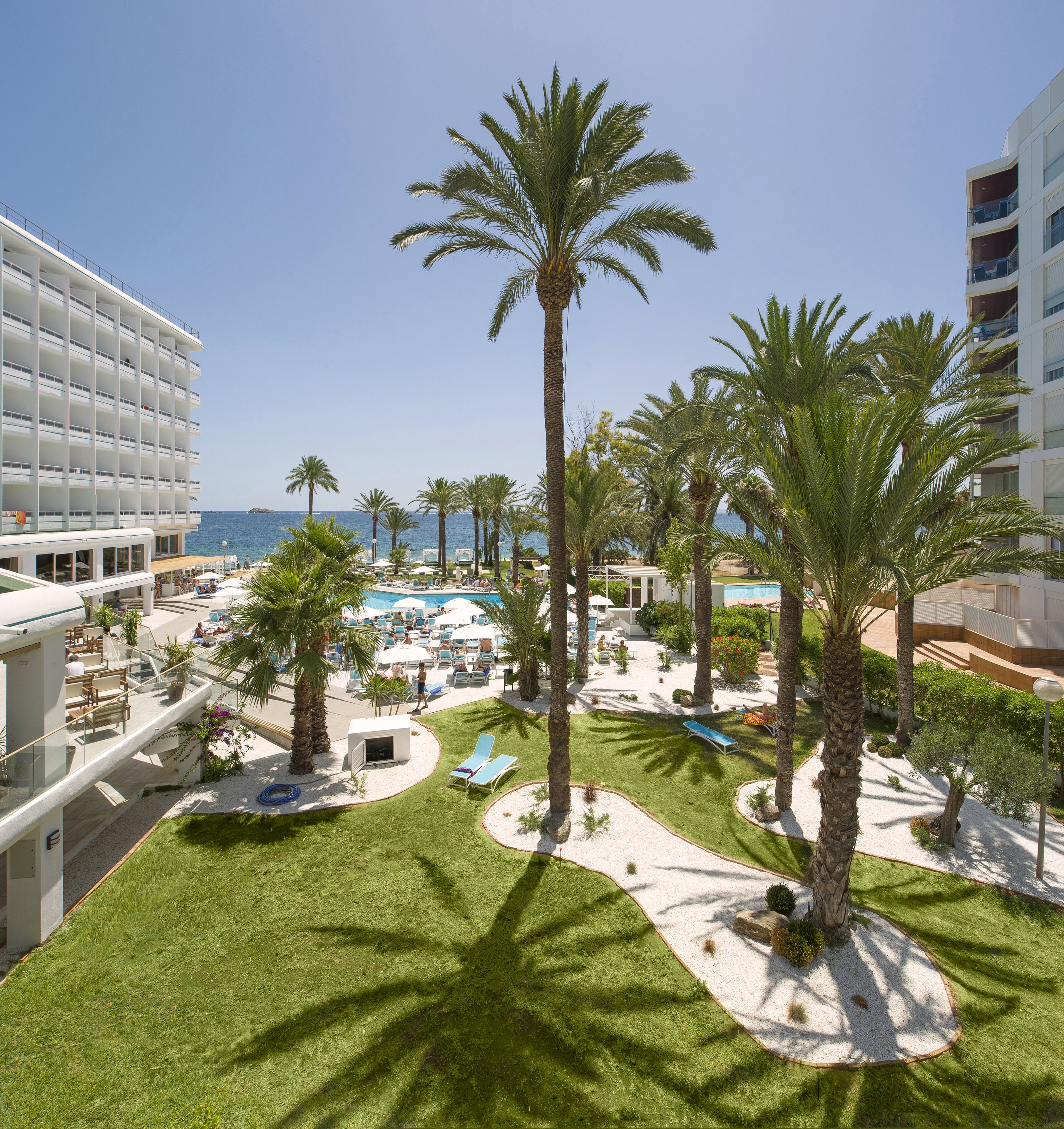 Un resort con zona de piscina, palmeras y vistas al mar.