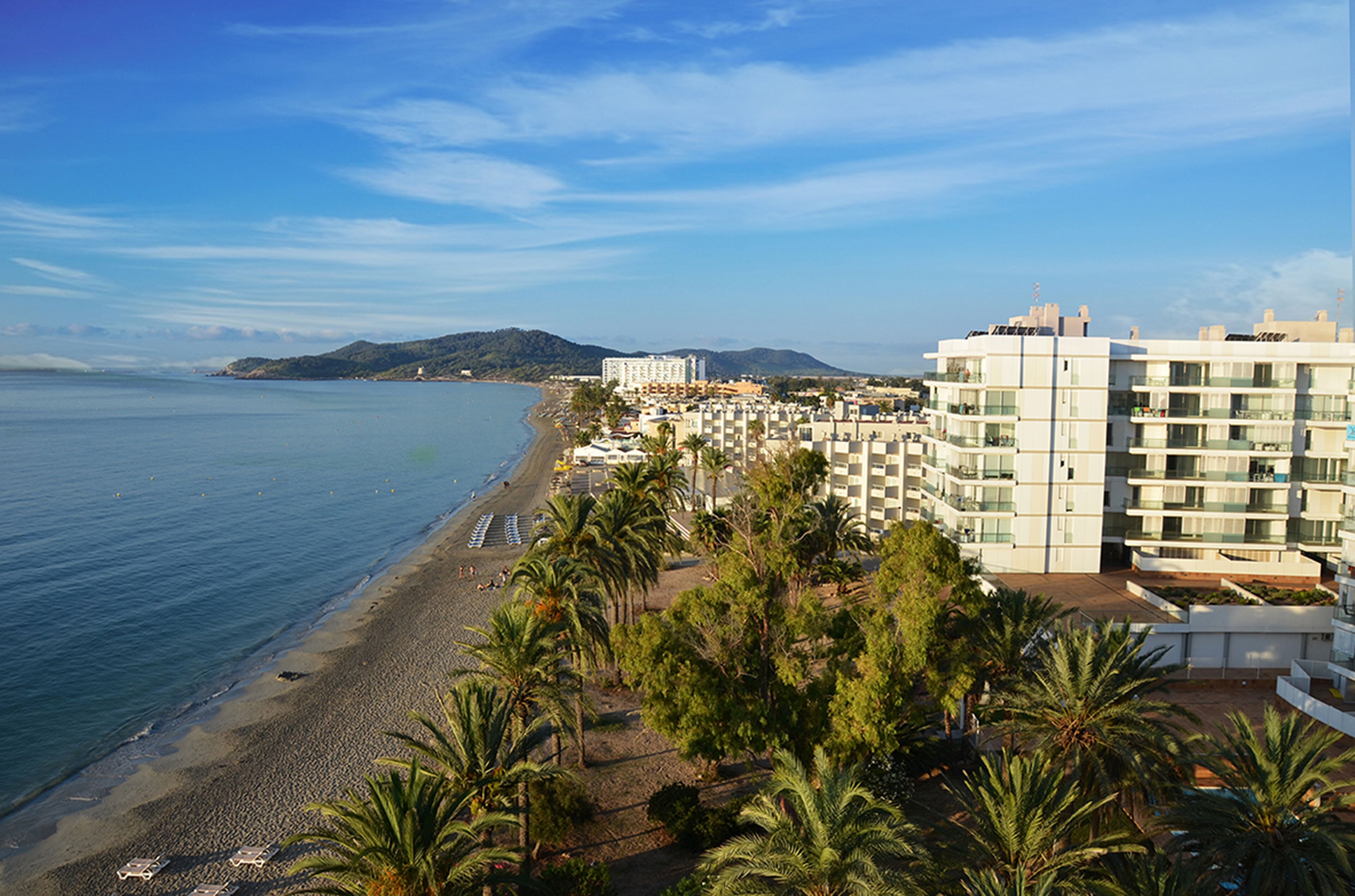 Un hotel frente al mar con vistas a la playa, varios pisos y una combinación de balcones y terrazas.