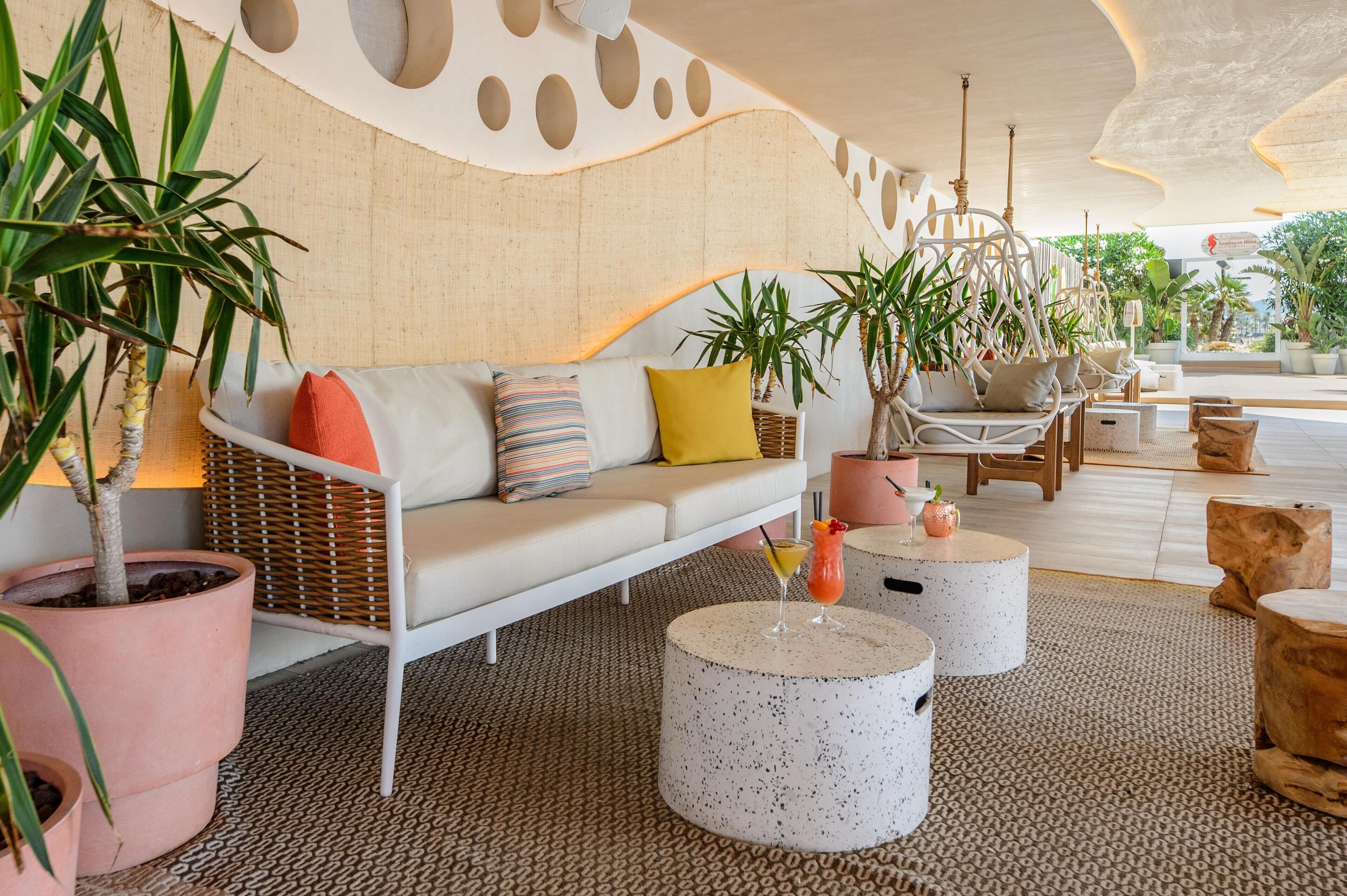 Un espace détente moderne avec un canapé blanc, des tables rondes et des plantes en pot.