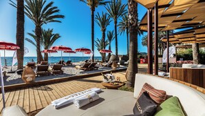 A beachside lounge area with sun loungers, umbrellas, and a wooden deck overlooking the sea. - Hotel Vibra Algarb (Ibiza Town)