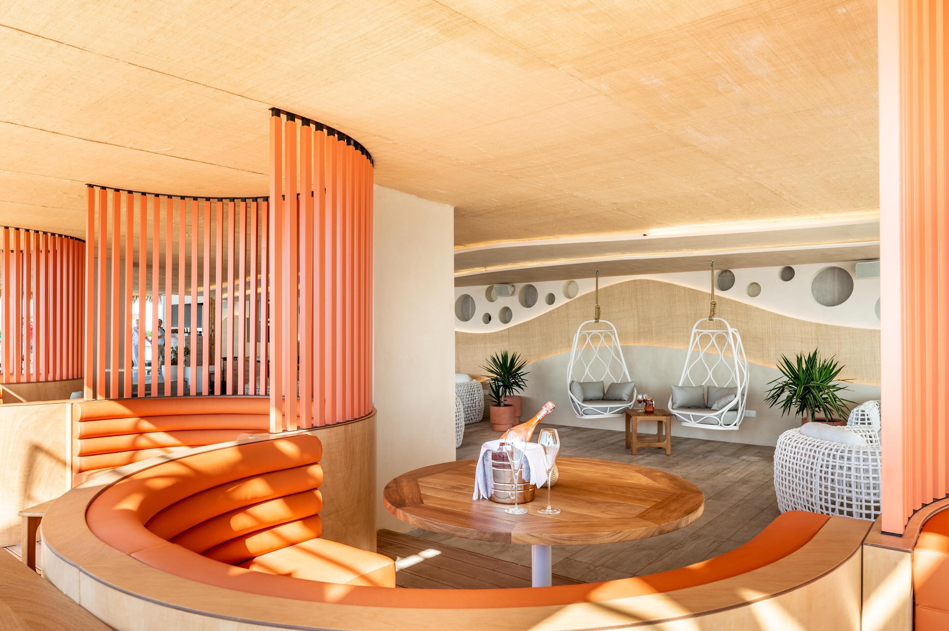 A modern interior with a curved wooden seating area, a round wooden table with a bottle and glass, and a hanging chair.