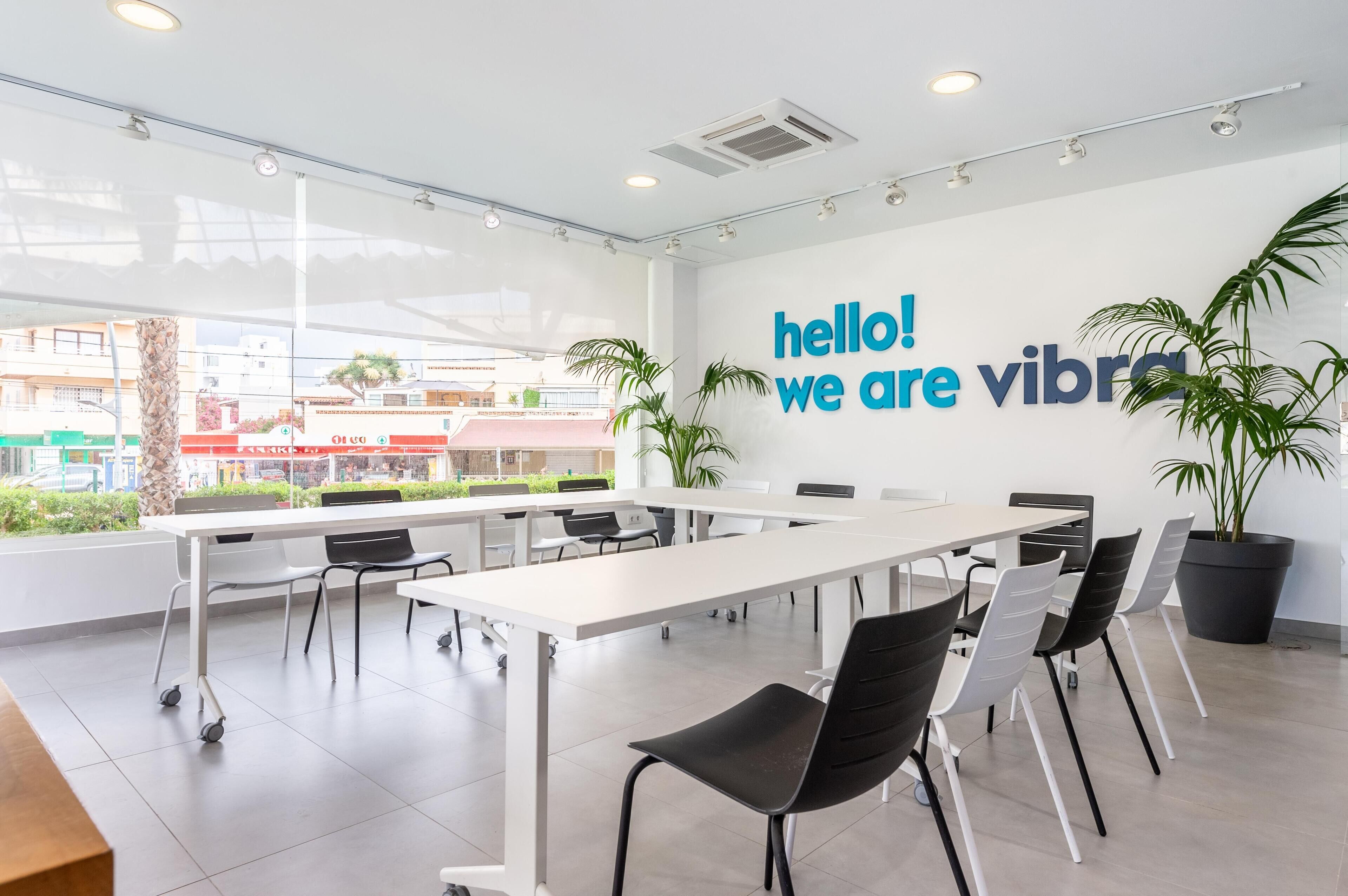 Une salle de conférence moderne, dotée d’une grande table, de chaises et d’une pancarte sur le mur indiquant : « Bonjour ! Nous sommes Vibra. »