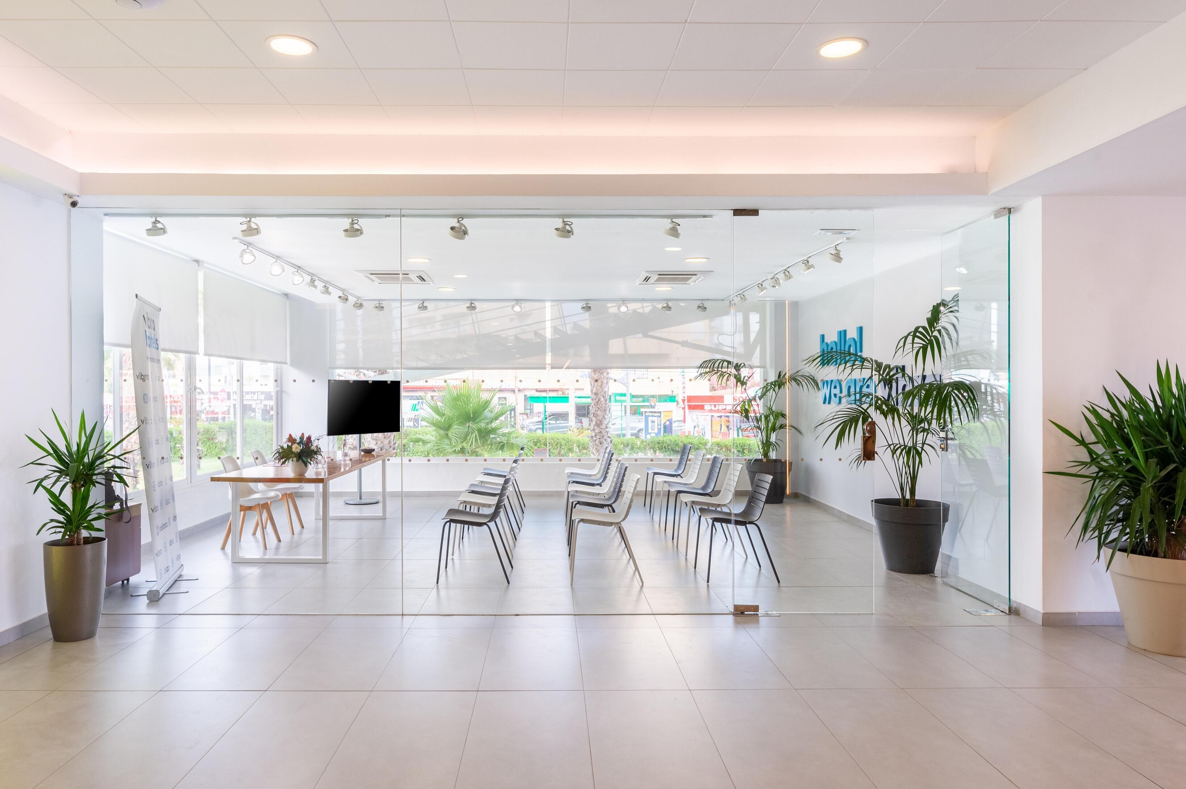 A modern waiting area with glass walls, a flat-screen TV, and several chairs.