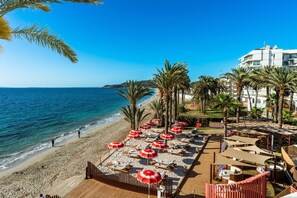 Un resort frente a la playa con tumbonas y sombrillas, una zona de piscina y vistas al mar.