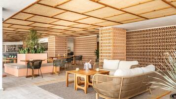 Een terras met houten tafels en stoelen, een rieten bank en een patroonwand.