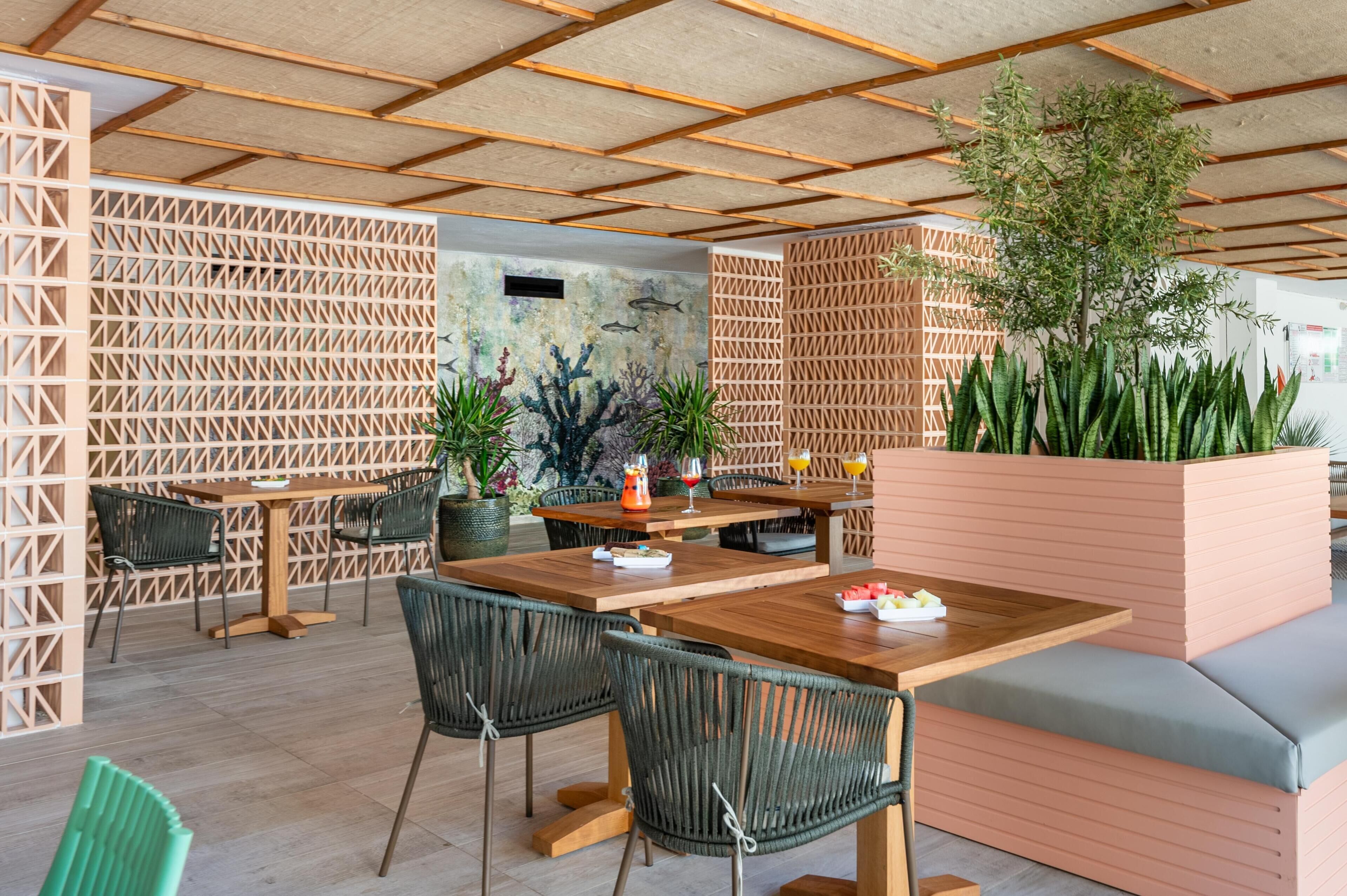 A modern outdoor dining area with wooden tables and chairs, surrounded by wooden lattice partitions and potted plants.