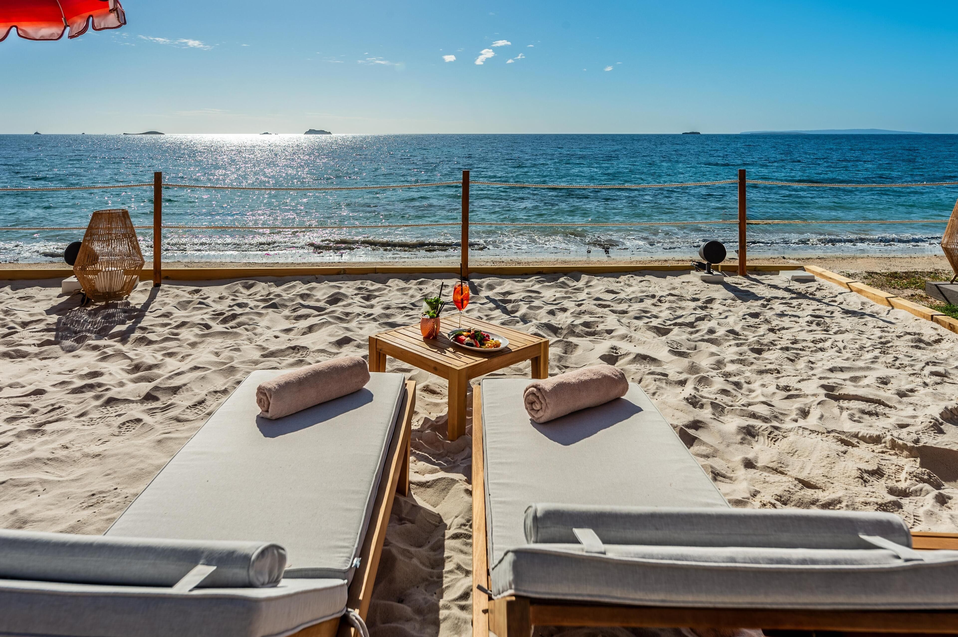 Een strandlounge met ligbedden, een tafel met drankjes en snacks, en uitzicht op de oceaan.