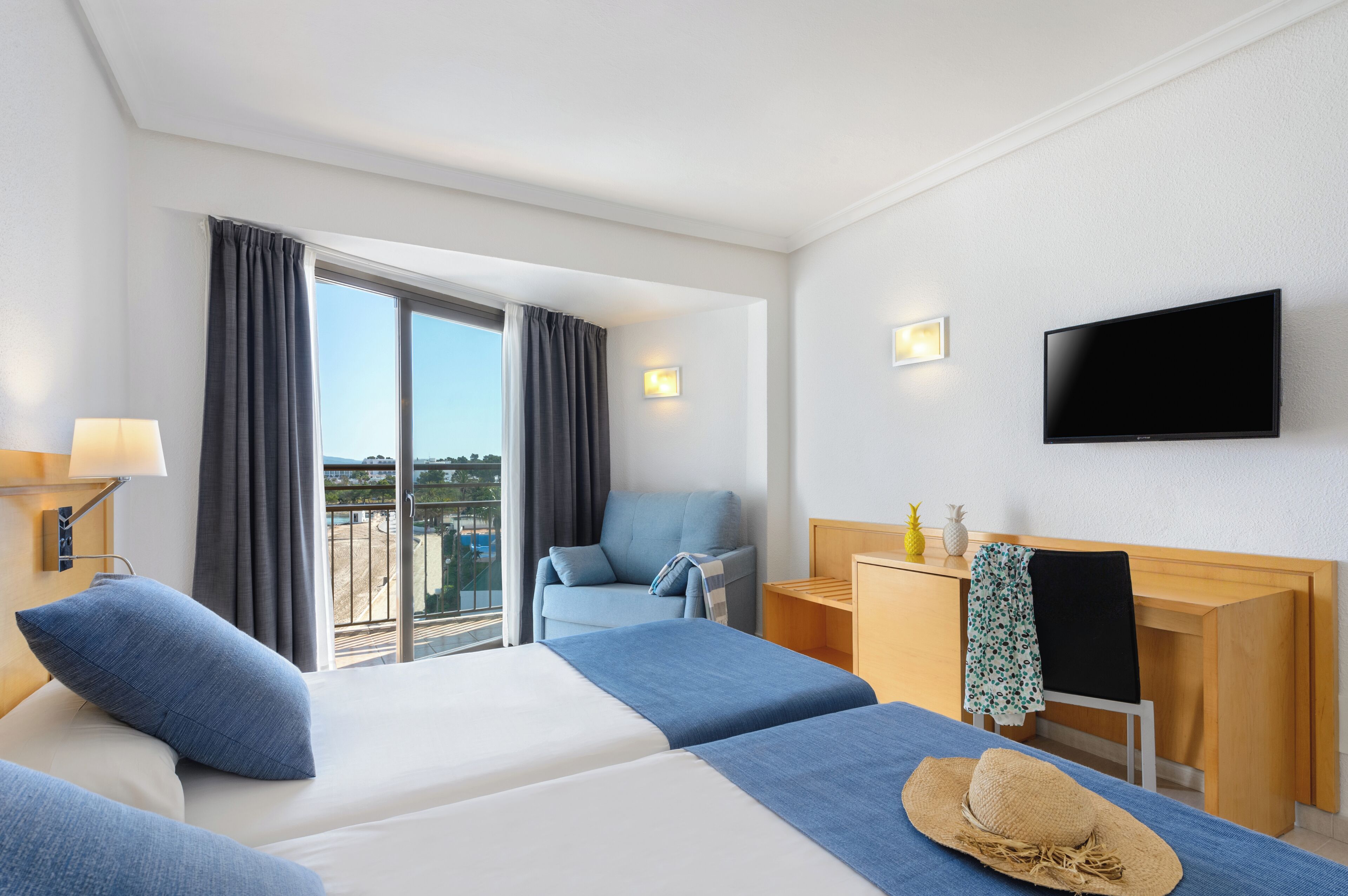 A hotel room with two beds, a desk, a TV, and a view of the city.