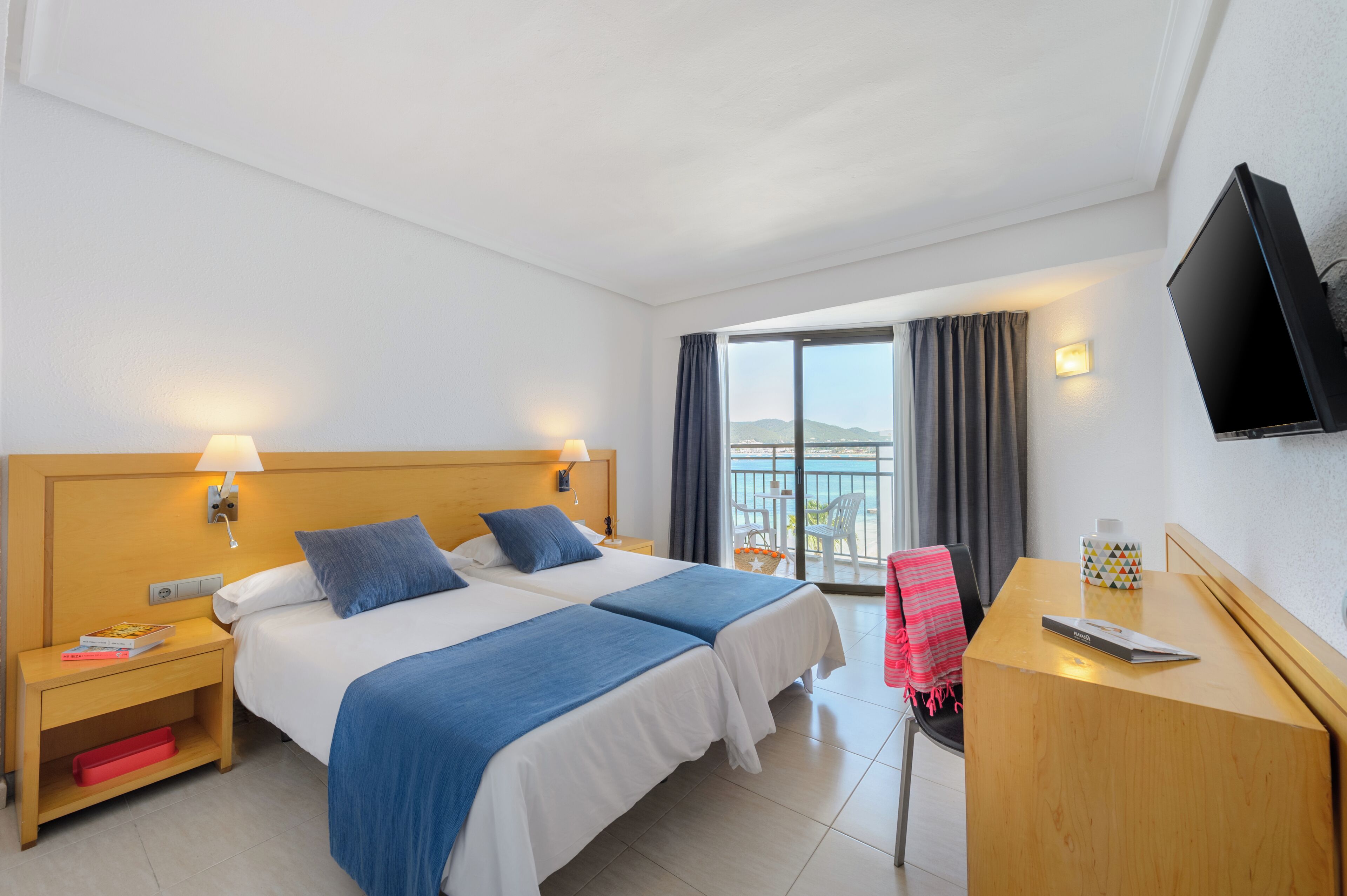 Habitación de hotel con dos camas, un escritorio, un televisor y un balcón con vistas.