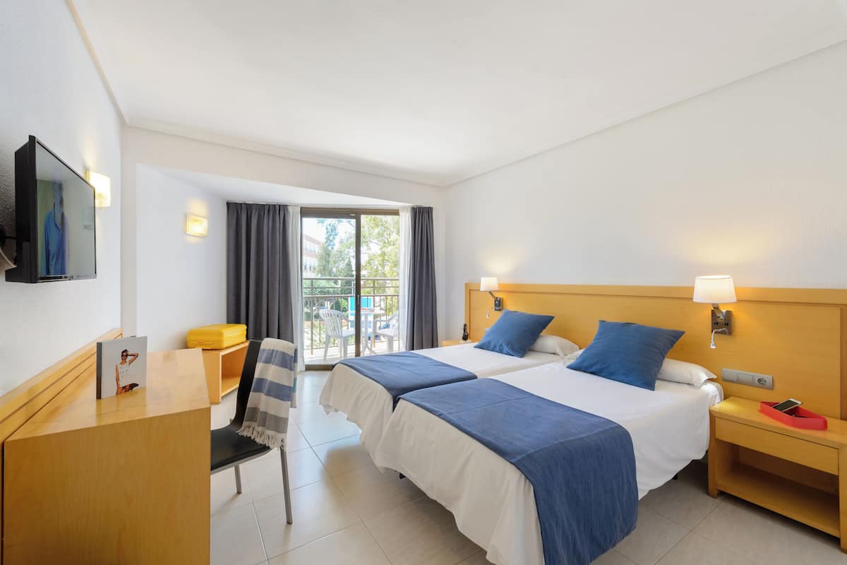 A hotel room with two beds, a desk, a chair, a TV, and a balcony with curtains.