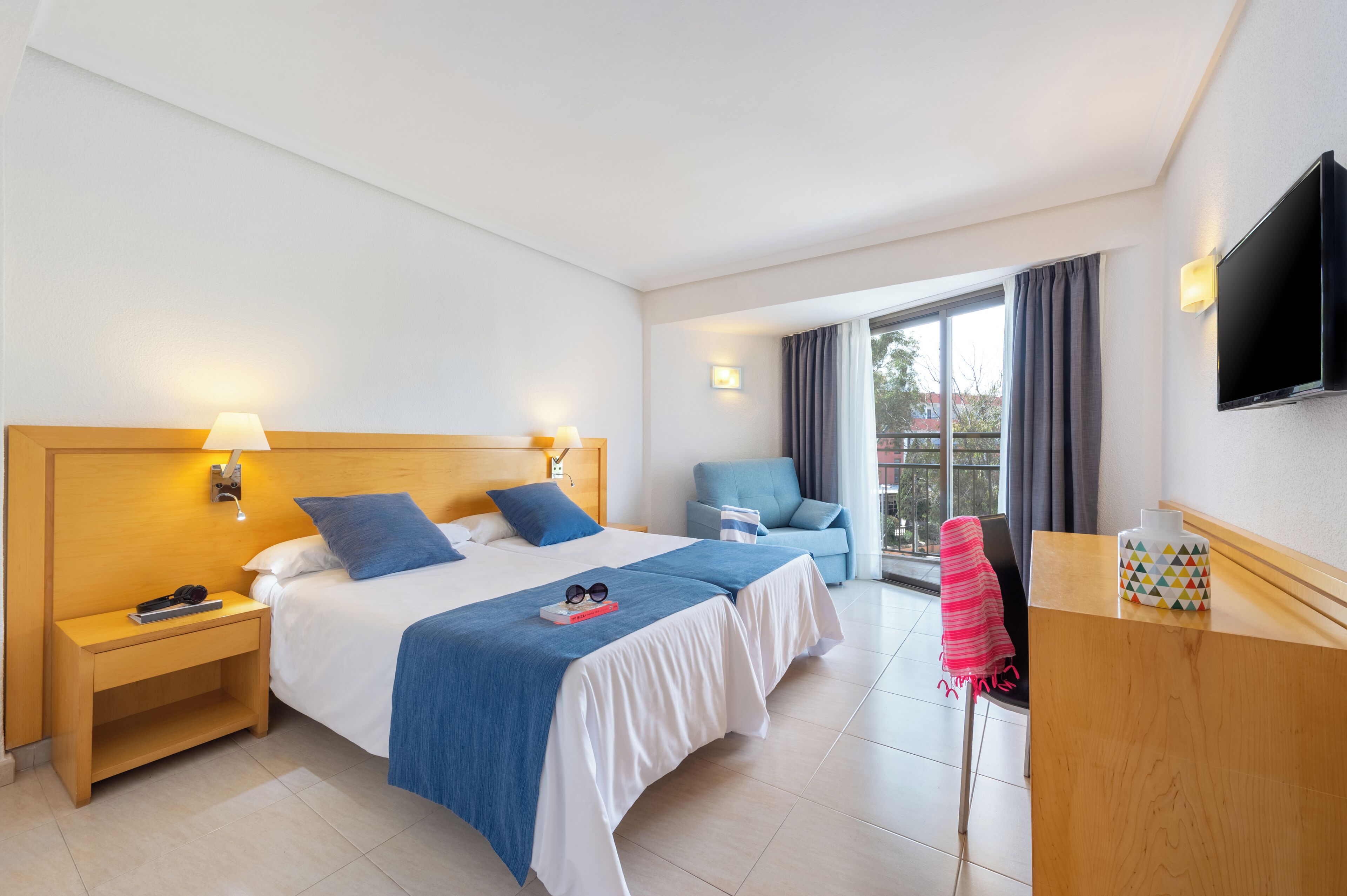 Una habitación de hotel con una cama grande, mesitas de noche, un televisor, un escritorio y una silla.