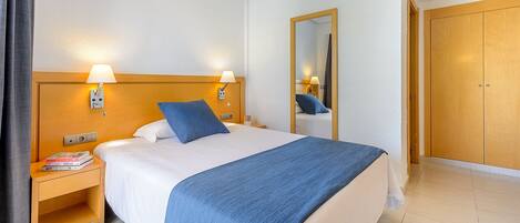 Una habitación de hotel con una cama, lámparas de noche, una mesita de noche, un espejo y un armario.