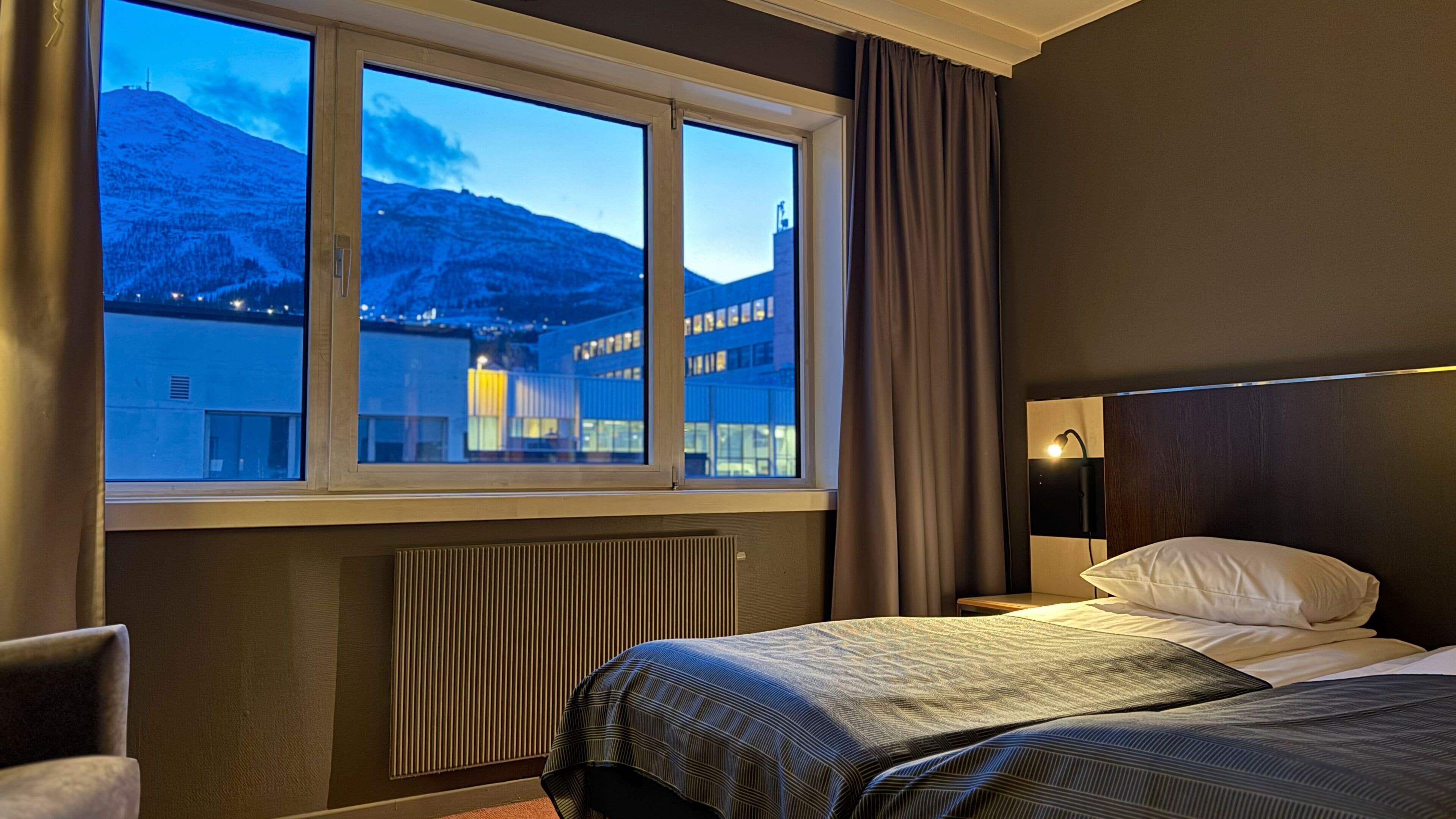 A hotel room with a large window offering a view of a mountain and buildings.