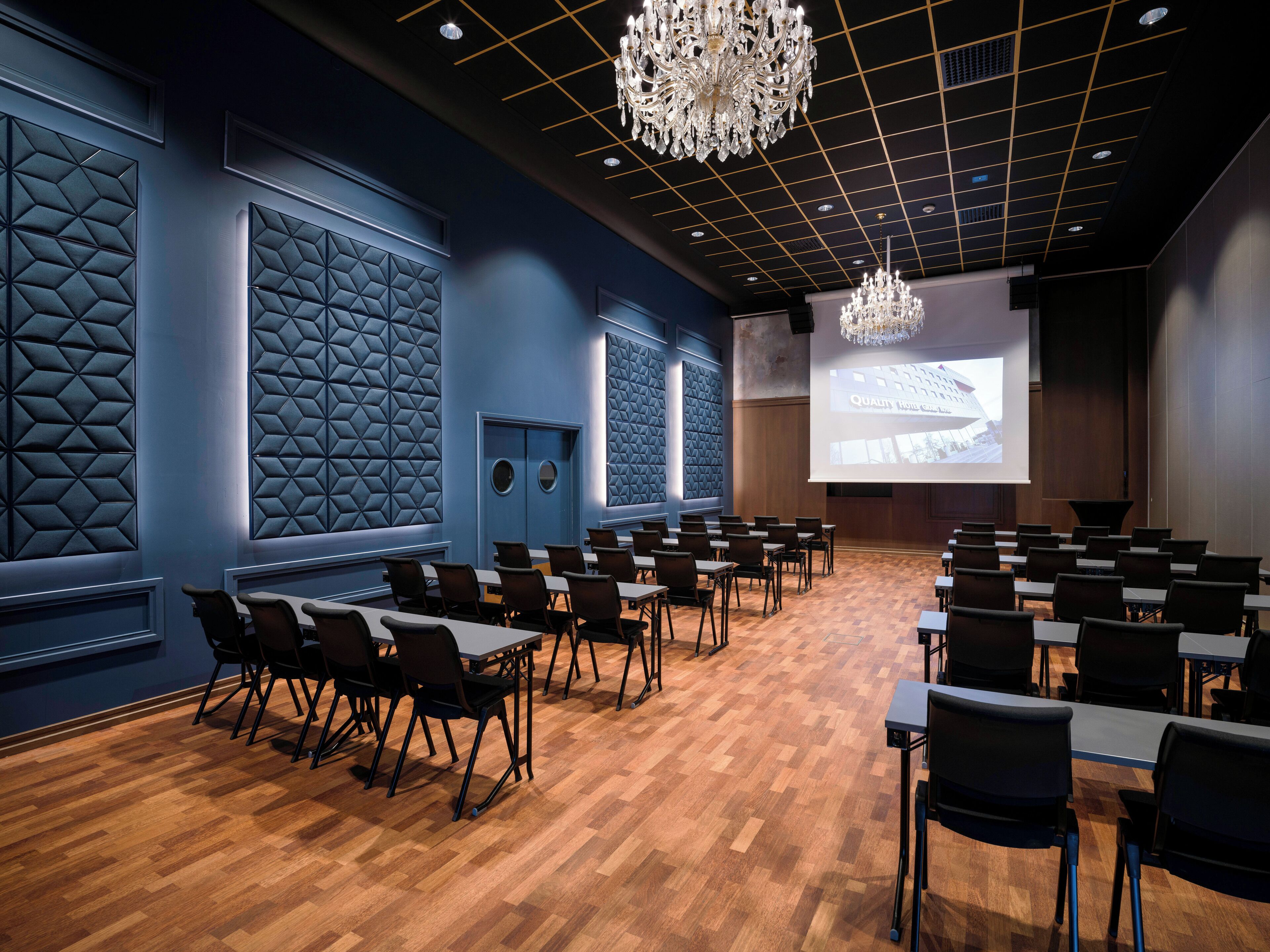 Sala de conferências com tela grande, piso de madeira e decoração moderna.