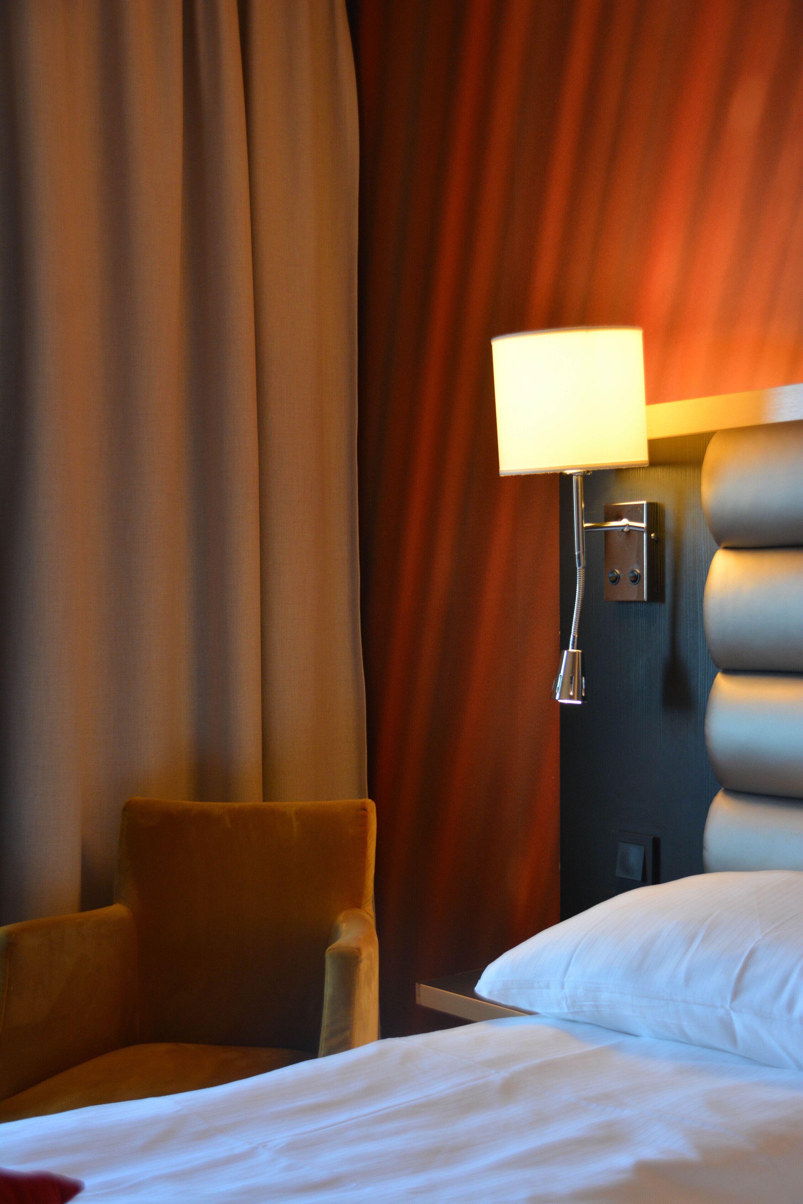Una habitación de hotel con una cama, una silla, una lámpara y cortinas.