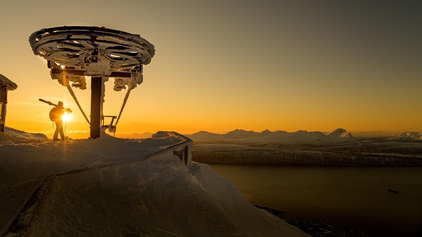 Une personne se tient à côté d’une grande structure mécanique, avec un paysage enneigé et des montagnes en arrière-plan.