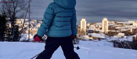 A child skiing on a snowy slope with a city and mountains in the background.