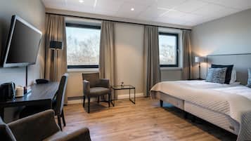 Habitación de hotel con cama, escritorio, silla, televisor y ventana con cortinas.