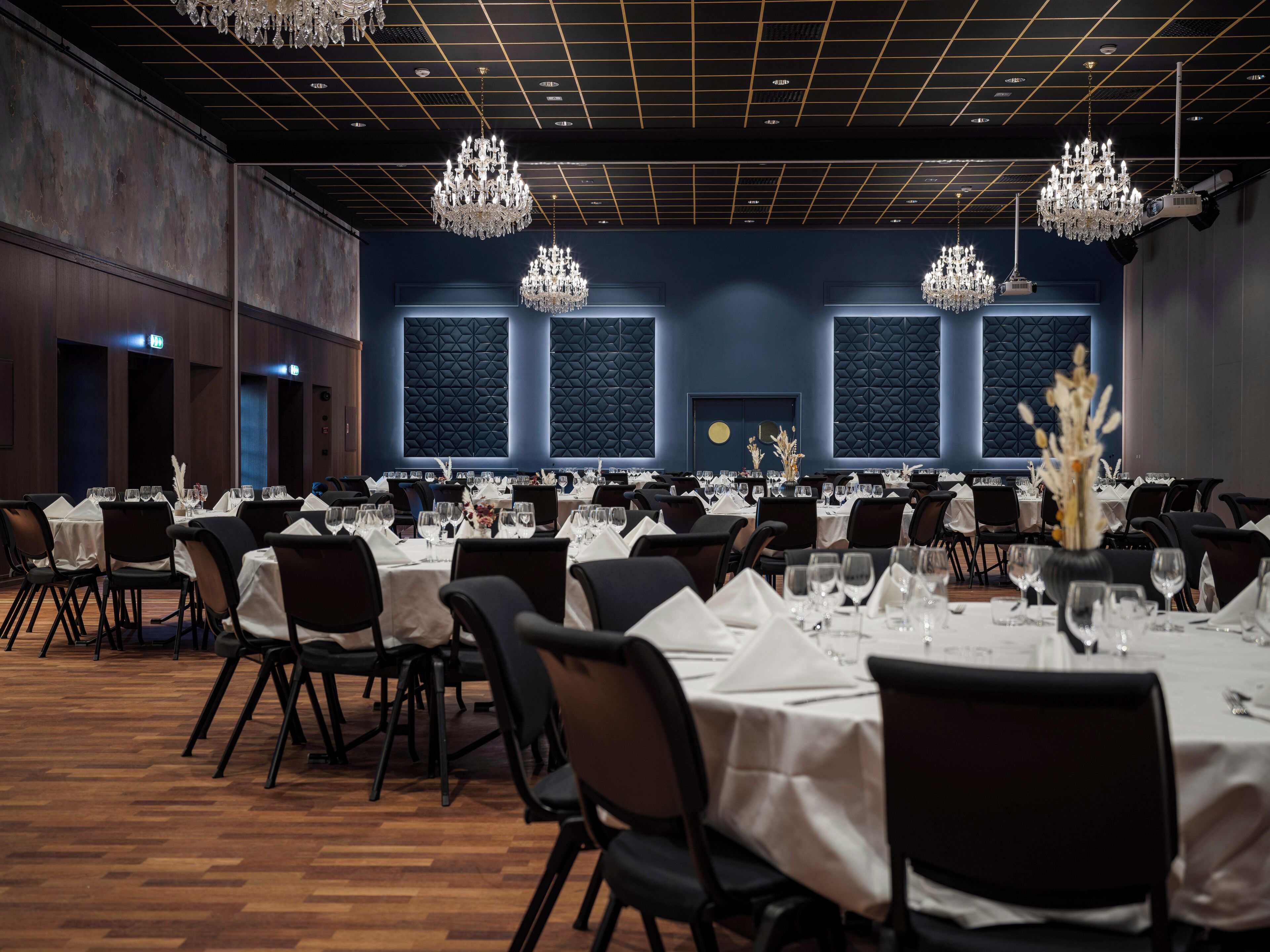 Ein großer Festsaal mit mehreren für das Essen gedeckten Tischen, ausgestattet mit Kristalllüstern und modernem Design.