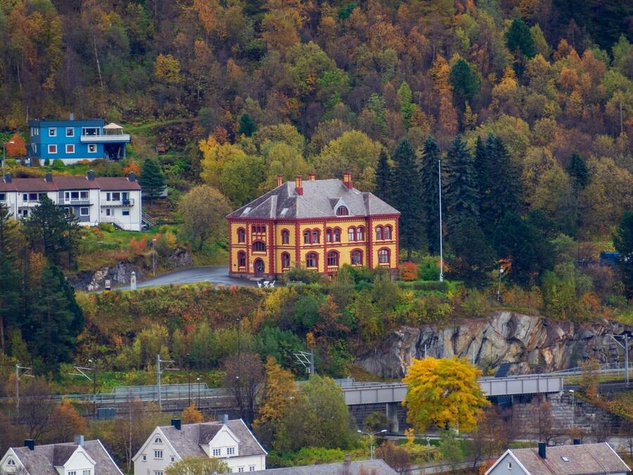 A red building with a symmetrical facade, surrounded by autumn foliage and residential houses.
