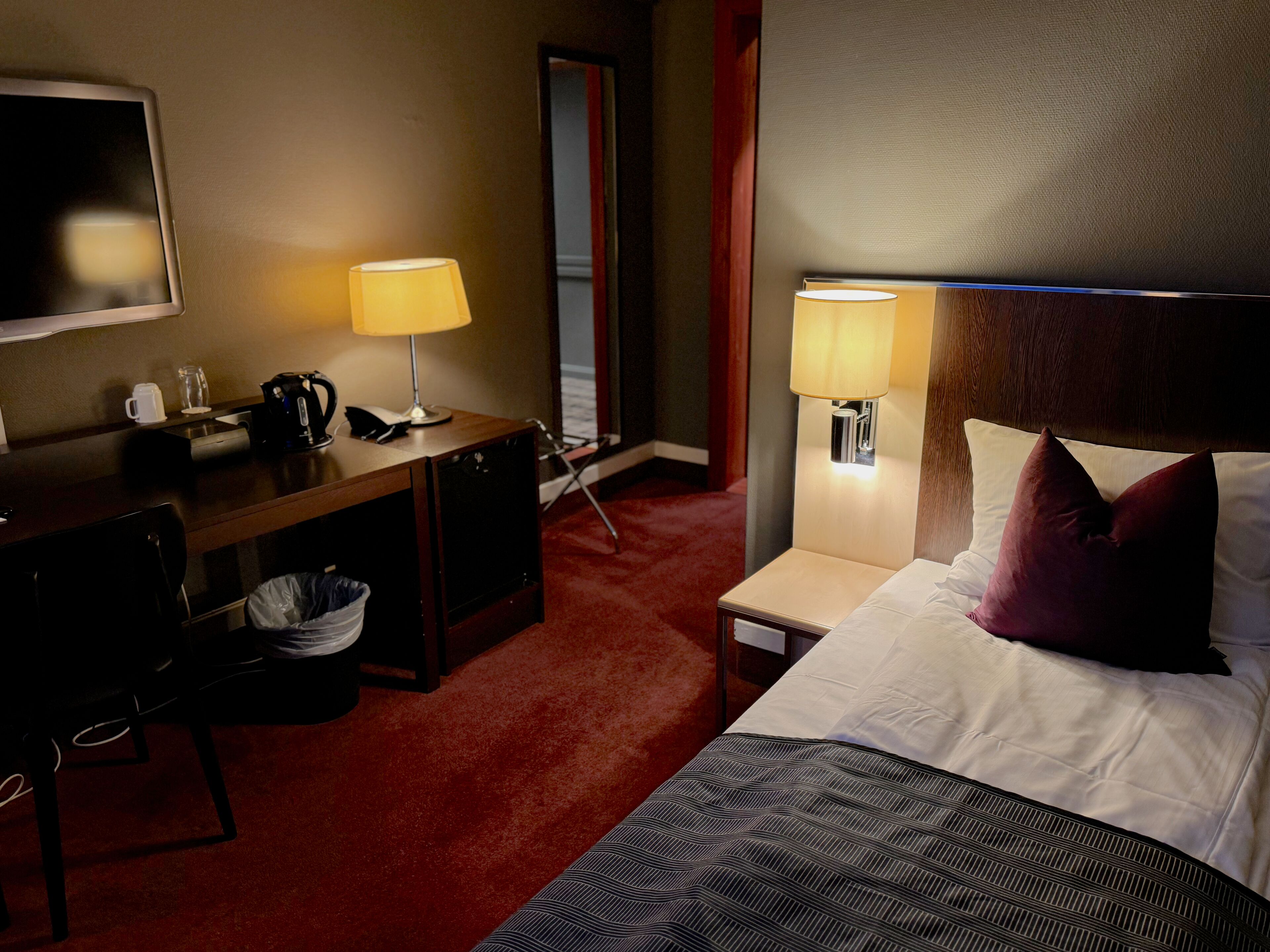 Quarto de hotel com cama, escrivaninha e duas luminárias de cabeceira.
