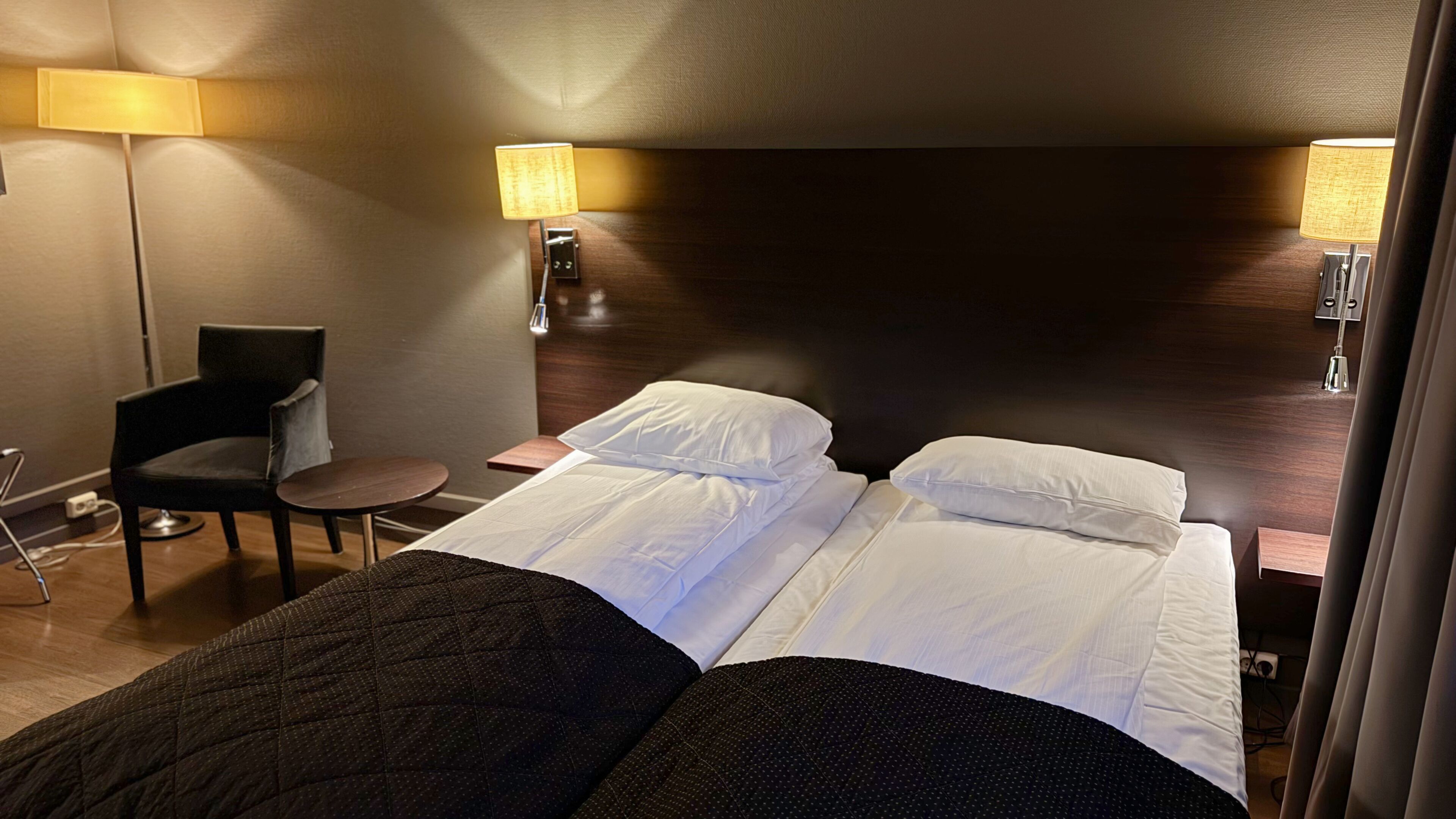 A hotel room with a bed, two bedside lamps, a chair, and a small table.
